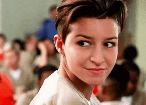 A Woman With Short Hair Is Smiling And Looking At The Camera In Front Of A Crowd . GIF