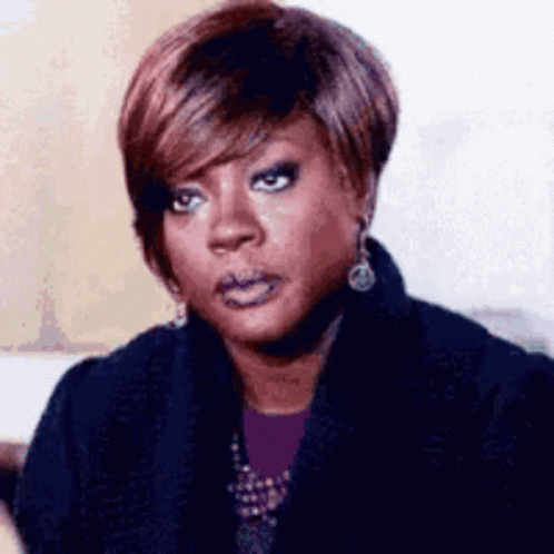A Woman With Short Hair Is Wearing A Black Coat And Earrings And Making A Funny Face . GIF