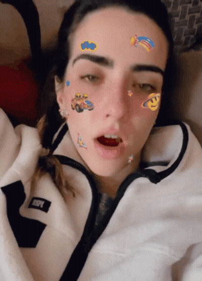 A Woman With Stickers On Her Face Is Wearing A White Jacket With The Letter R On The Front GIF