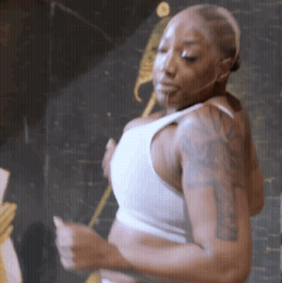 A Woman With Tattoos On Her Arms Is Wearing A White Tank Top And Dancing . GIF