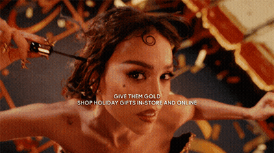 A Woman With The Words Give Them Gold Shop Holiday Gifts In Store And Online Above Her GIF