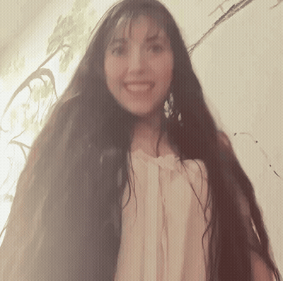 A Woman With Very Long Hair Is Smiling And Looking At The Camera GIF
