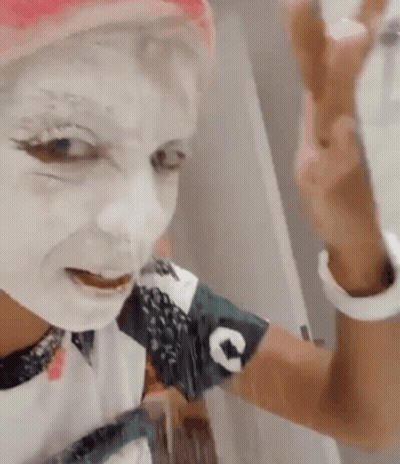 A Woman With White Paint On Her Face Is Taking A Selfie With Her Phone . GIF