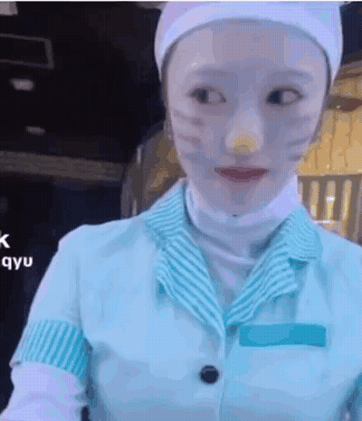 A Woman With White Paint On Her Face Is Wearing A Blue And White Uniform And A White Hat . GIF