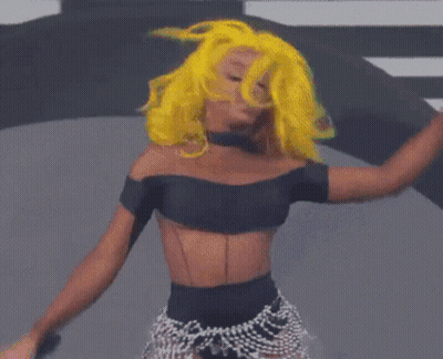 A Woman With Yellow Hair Is Dancing In Front Of A Colorful Backdrop GIF