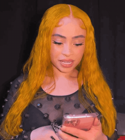 A Woman With Yellow Hair Is Holding A Cell Phone In Her Hand GIF