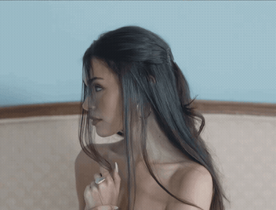 A Woman Without A Shirt Is Sitting On A Couch With Her Hair In A Ponytail GIF