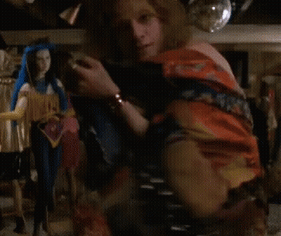 A Woman Without A Shirt Is Standing In Front Of A Shelf With Dolls On It . GIF