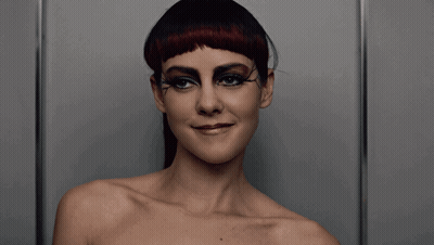 A Woman Without A Shirt Is Wearing Black Eye Shadow And Red Hair GIF