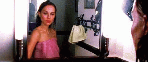 A Woman Wrapped In A Pink Towel Is Standing In Front Of A Mirror . GIF
