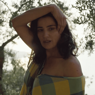 A Woman Wrapped In A Plaid Shirt Is Standing In Front Of A Tree GIF