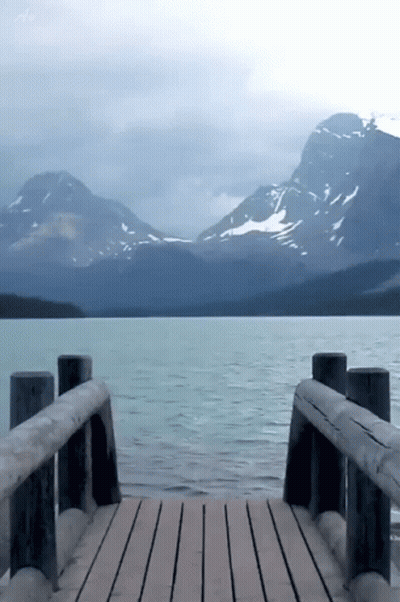 A Wooden Dock With Mountains In The Background And A Lake In The Foreground GIF