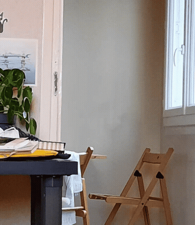 A Wooden Folding Chair Sits Next To A Desk With A Picture On The Wall Above It GIF