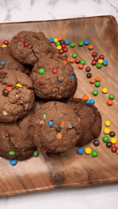 A Wooden Plate Topped With Chocolate Cookies And M & Ms GIF