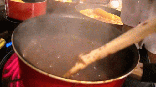 A Wooden Spoon Is Stirring A Pot Of Liquid GIF