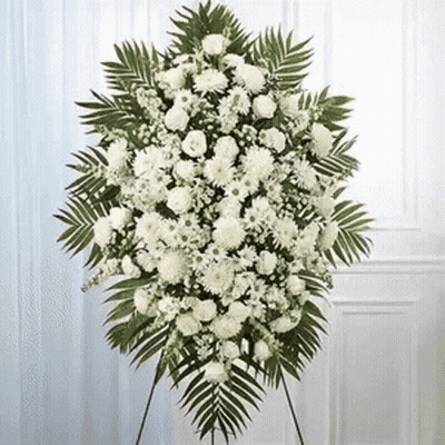 A Wreath Of White Flowers And Green Leaves Is Sitting On A Stand In Front Of A Door . GIF