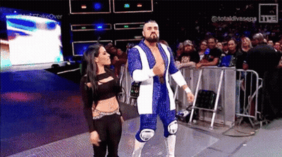 A Wrestler And A Woman Are Walking On A Stage . GIF