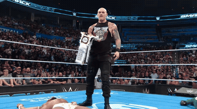 A Wrestler Holds A Trophy In A Wrestling Ring With A Crowd Watching GIF