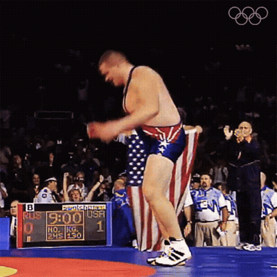 A Wrestler Holds An American Flag In Front Of A Scoreboard That Says " Bud Light " On It GIF