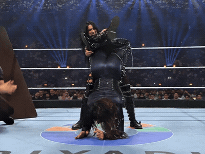 A Wrestler Holds Another Wrestler Upside Down On Her Back GIF