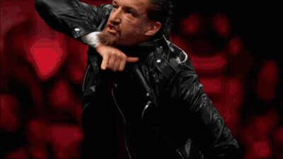 A Wrestler In A Black Leather Jacket Raises His Hand GIF
