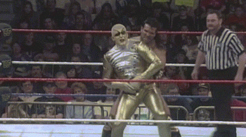 A Wrestler In A Gold Bodysuit Is Standing In A Ring GIF