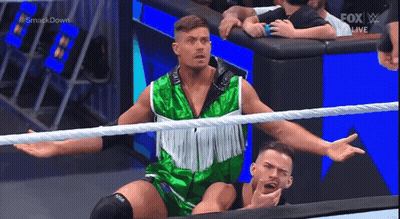 A Wrestler In A Green And White Outfit Is Standing In A Wrestling Ring . GIF