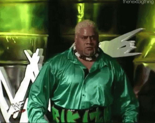 A Wrestler In A Green Shirt Stands In Front Of A Sign That Says The Next Big Thing GIF