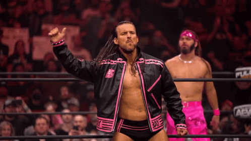 A Wrestler In A Pink And Black Jacket Stands In A Ring With Two Other Men GIF
