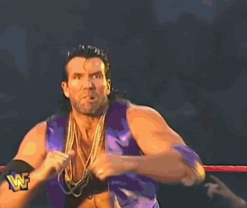 A Wrestler In A Purple Vest And Gold Chains Is Standing In A Ring With A Wf Logo On The Bottom GIF
