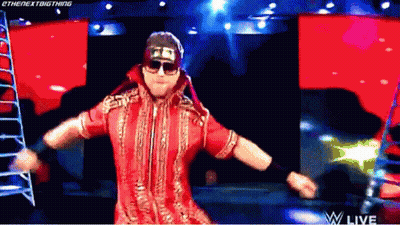 A Wrestler In A Red Outfit And Sunglasses Is Dancing On A Stage . GIF