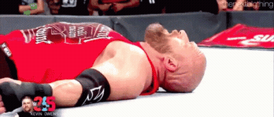 A Wrestler In A Red Shirt Is Laying Down On The Ground GIF