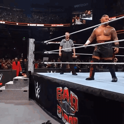 A Wrestler In A Ring With A Referee And A Banner That Says Bad Blood GIF