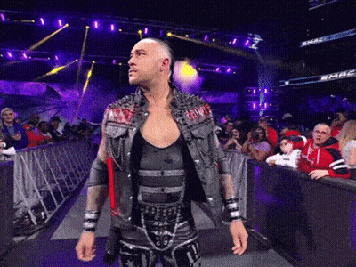 A Wrestler In A Studded Vest Stands In Front Of A Crowd At A Wrestling Match GIF