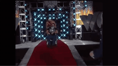 A Wrestler In A Wheelchair Is Sitting On A Red Carpet On A Stage . GIF
