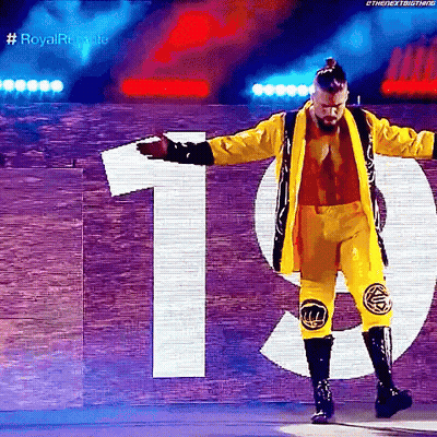 A Wrestler In A Yellow Jacket And Pants Is Standing In Front Of A Sign That Says 19 . GIF