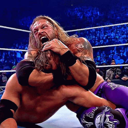 A Wrestler In Purple Shorts Is Wrestling Another Wrestler In A Ring GIF