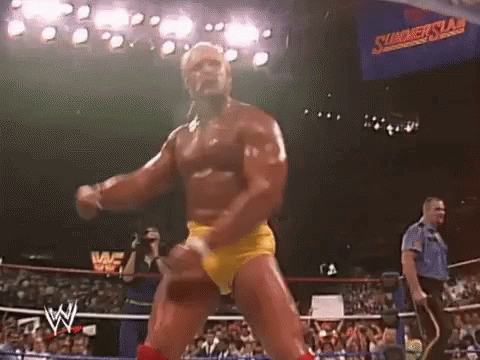 A Wrestler In Yellow Shorts Is Dancing In A Wrestling Ring In Front Of A Crowd . GIF