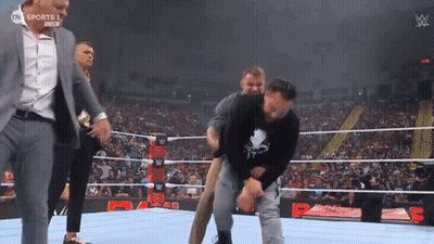 A Wrestler Is Being Helped Out Of The Ring By A Man In A Suit GIF