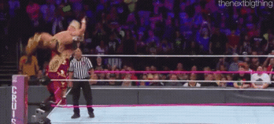A Wrestler Is Being Lifted In The Air By A Referee In A Wrestling Ring While A Crowd Watches . GIF