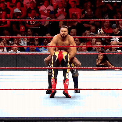 A Wrestler Is Carrying Another Wrestler In A Wrestling Ring While A Crowd Watches GIF