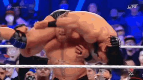 A Wrestler Is Carrying Another Wrestler On His Back In A Ring . GIF