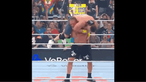 A Wrestler Is Carrying Another Wrestler On His Back In A Wrestling Ring . GIF