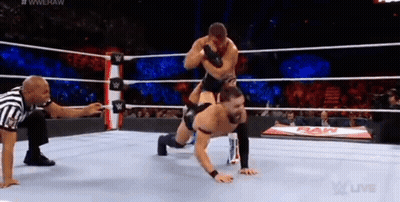 A Wrestler Is Doing Push Ups In A Wrestling Ring While A Referee Looks On . GIF