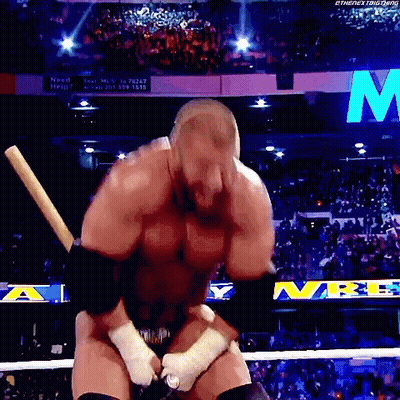 A Wrestler Is Holding A Baseball Bat In A Wrestling Ring With The Letter M In The Background GIF