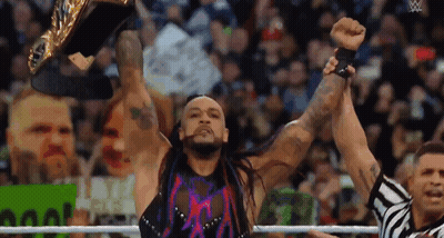 A Wrestler Is Holding A Championship Belt In The Air While A Referee Looks On . GIF
