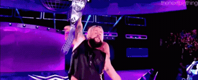 A Wrestler Is Holding A Championship Belt In The Air While Standing On A Stage . GIF