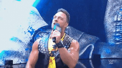 A Wrestler Is Holding A Microphone In His Hand And Talking Into It On A Stage . GIF