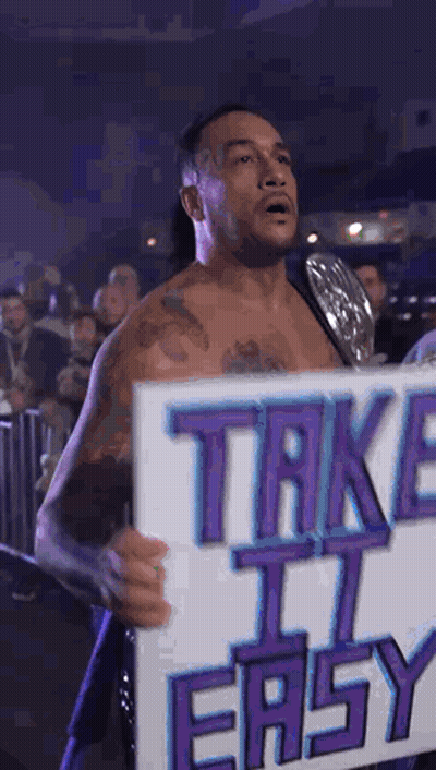 A Wrestler Is Holding A Sign That Says Take It Easy . GIF
