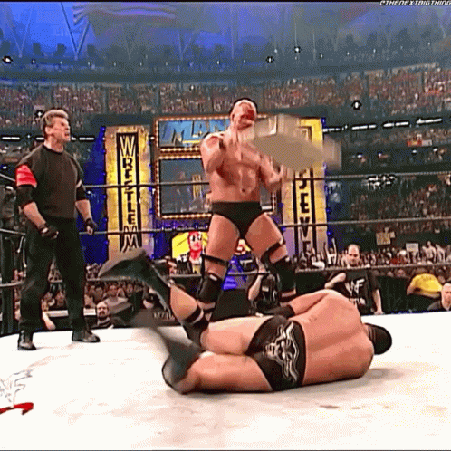 A Wrestler Is Holding A Trophy While Another Wrestler Is Laying On The Floor GIF